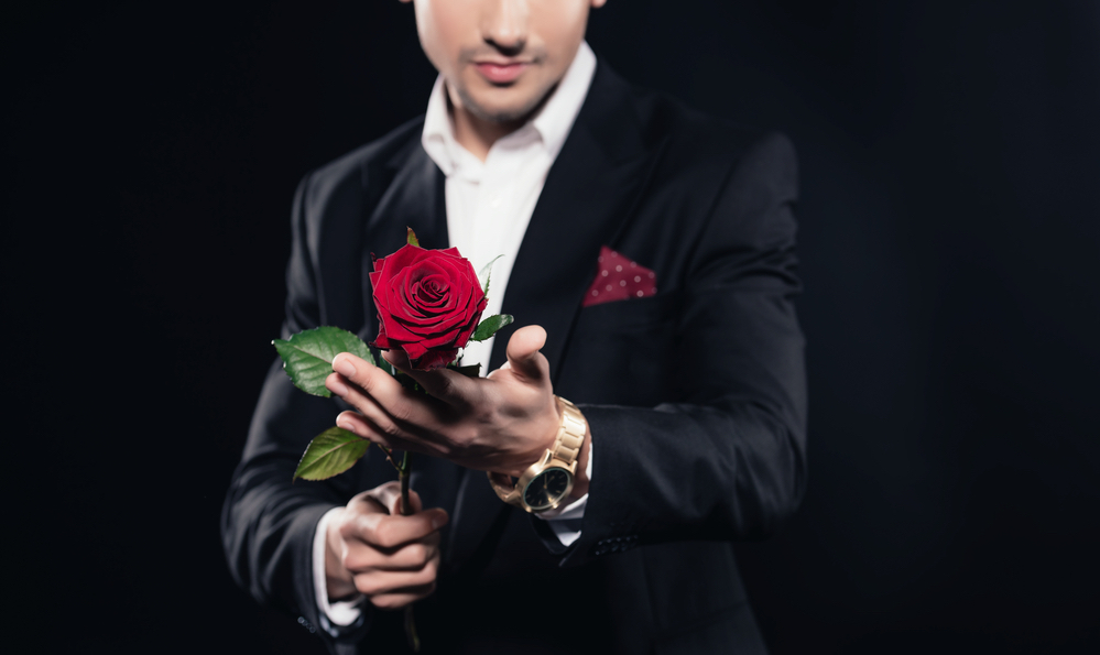 Stock photo of a man in a suit wearing a red pocket square and holding a red rose.