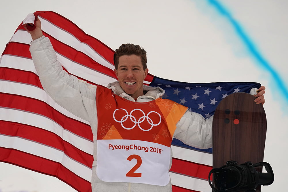 Shaun White wears sweatshirt uniform while holding snowboard and American flag in 2018 Olympics. Photo by Deposit Photos user zhukovsky